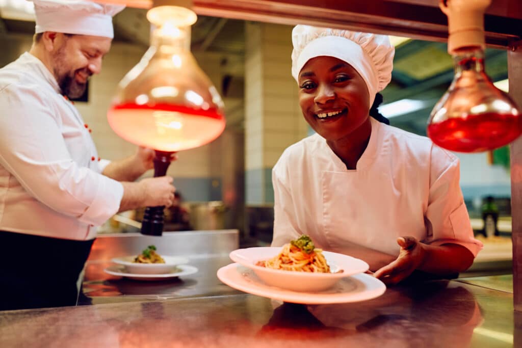 Mala Barad smiling while serving a spaghetti dish at the kitchen pass